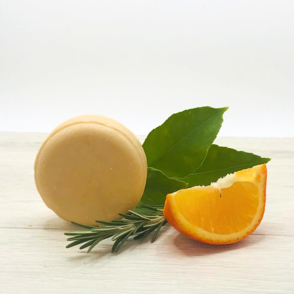 DOCTOR DERMA Vital Hair Boost Shampoo: Festes 2-in-1 Shampoo & Conditioner gegen Haarbruch und Haarverlust auf Holz. Dekoriert mit einem frischen Rosmarinzweig, einer Orangenscheibe und grünen Blättern. Kräftigende, plastikfreie Haarpflege mit Koffein und Arganöl.