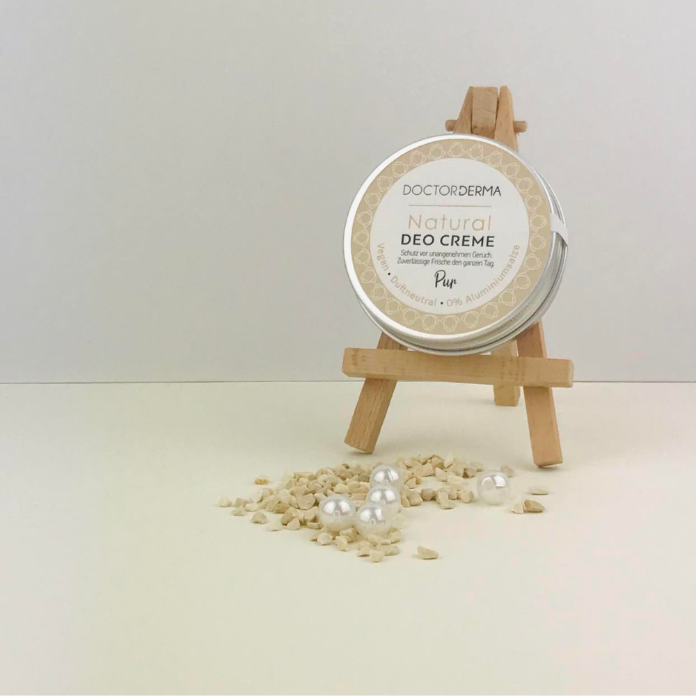 DOCTOR DERMA Natural Deo Creme Pur duftneutral auf einer Mini-Holzstaffelei, dekoriert mit feinen Dekosteinen und weißen Perlen vor hellem Hintergrund. Extra sensitives Naturkosmetik-Deo ohne Aluminiumsalze und Duftstoffe für Allergiker.